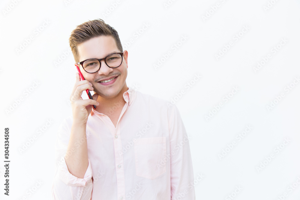 Happy cheerful guy in eyeglasses chatting on cellphone. Young man in glasses standing isolated over white background. Mobile communication concept Happy cheerful guy in eyeglasses chatting on cellphone. Young man in glasses standing isolated over white background. Mobile communication concept