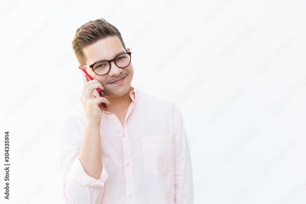 Positive friendly guy in eyewear talking on cellphone. Young man in glasses standing isolated over white background. Communication concept Positive friendly guy in eyewear talking on cellphone. Young man in glasses standing isolated over white background. Communication concept