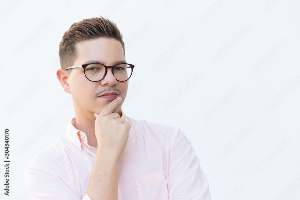 Closeup of pensive serious guy in eyewear touching chin and looking at camera. Young man in glasses standing isolated over white background. Decision making concept Closeup of pensive serious guy in eyewear touching chin and looking at camera. Young man in glasses standing isolated over white background. Decision making concept