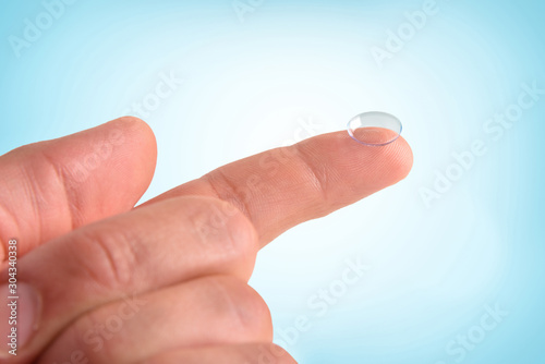 Hand with contact lens on finger with isolated blue background