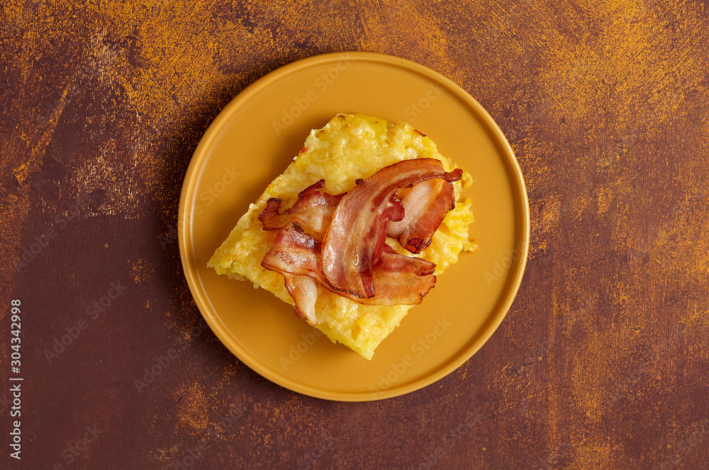 Cheesy potato bake with fried bacon on yellow plate. Overhead view