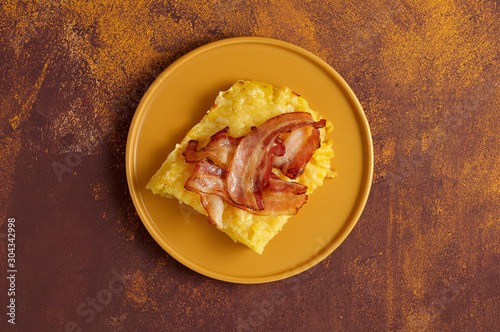 Obraz na płótnie Cheesy potato bake with fried bacon on yellow plate. Overhead view w salonie