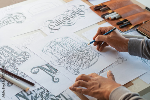 Typography Calligraphy artist designer drawing sketch writes letting spelled pen brush ink paper table artwork.Workplace design studio. photo