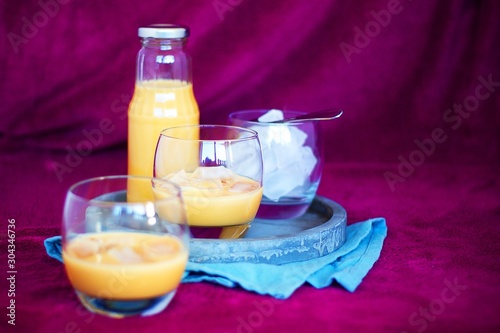 Homemade caramel alcohol drink served in pure glass with ice cubes on concrete tray and blue cloth with purple background