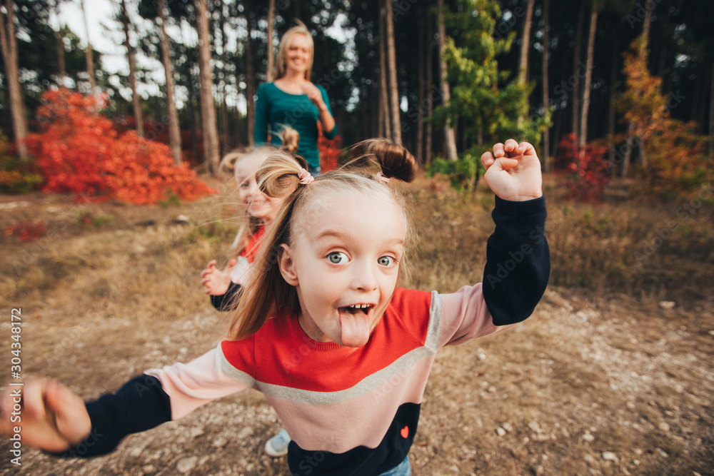 Blonde mother and her twin daughters are walking in the autumn forest among red trees. Blonde mother and her twin daughters are walking in the autumn forest among red trees.