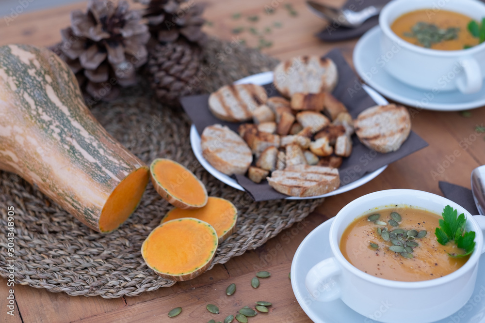 Healthy eating in autumn and winter time. Wooden table with two bowls of pumpkin cream soup. In the middle of the table bread croutons. Healthy eating in autumn and winter time. Wooden table with two bowls of pumpkin cream soup. In the middle of the table bread croutons.