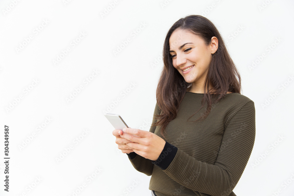 Smiling positive cellphone user texting message. Young woman in casual with mobile phone standing isolated over white background. Internet app concept Smiling positive cellphone user texting message. Young woman in casual with mobile phone standing isolated over white background. Internet app concept