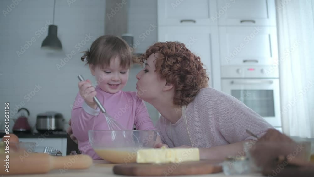 Parent plays with the child in the cook. Mom kisses her daughter while cooking. The child kneads the dough in the kitchen under the supervision of mom. Parent plays with the child in the cook. Mom kisses her daughter while cooking. The child kneads the dough in the kitchen under the supervision of mom.