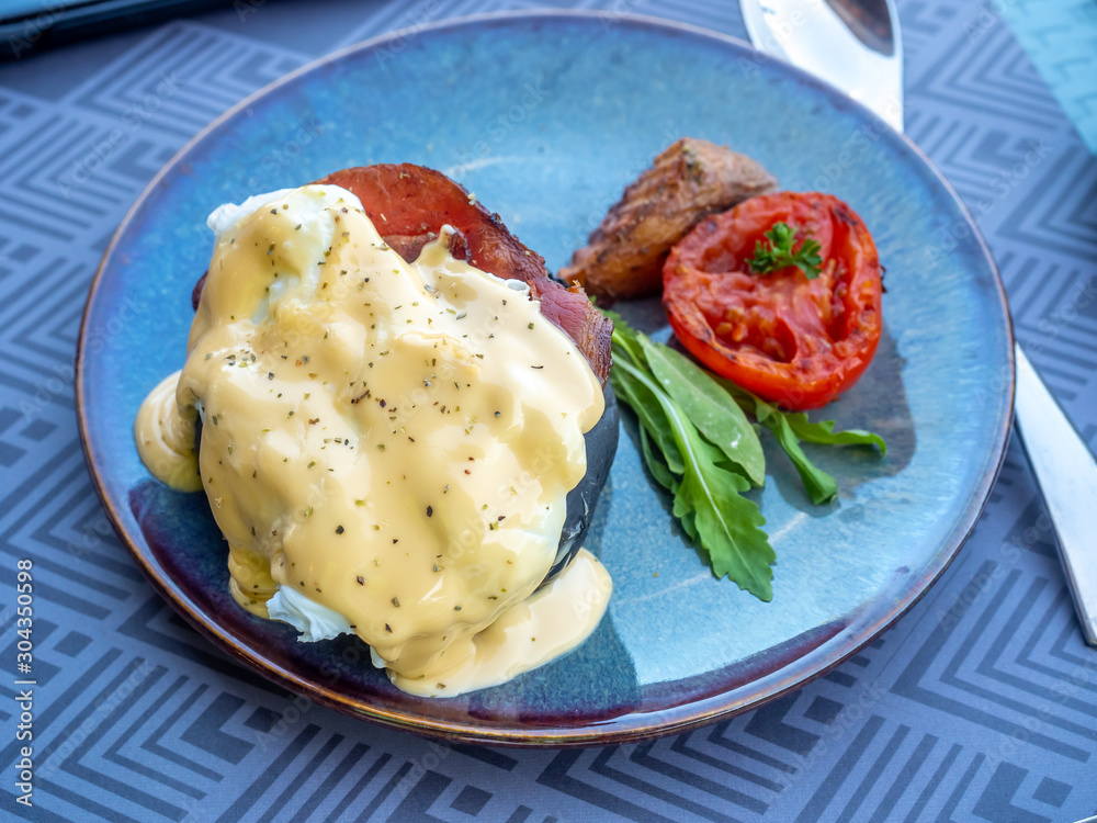 Poached egg benedict served with potato, tomato and spinach on black dish for breakfast Poached egg benedict served with potato, tomato and spinach on black dish for breakfast
