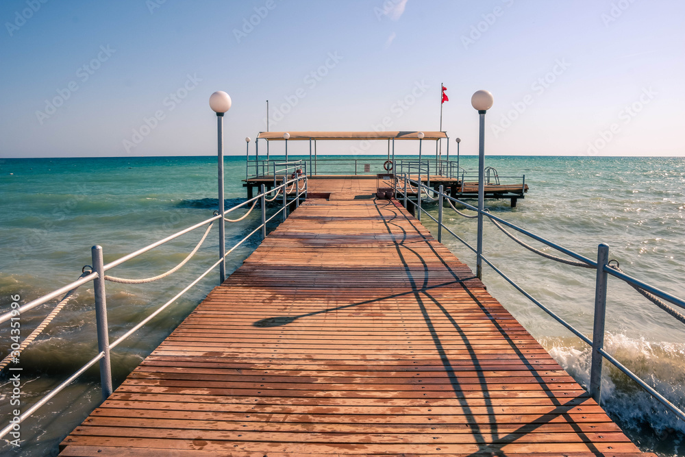 The pier goes into perspective against the background of the sea and the blue sky. White sand on the beach