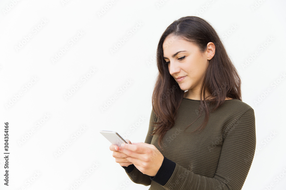 Focused serious cellphone user texting message. Young woman in casual with mobile phone standing isolated over white background. Wireless technology concept Focused serious cellphone user texting message. Young woman in casual with mobile phone standing isolated over white background. Wireless technology concept
