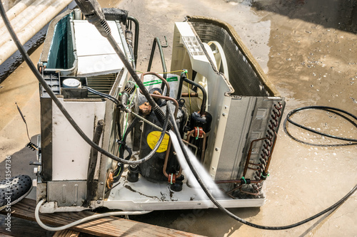 a professional electrician is cleaning the window air conditioner on the roof top of a house with his high pressure water gun 