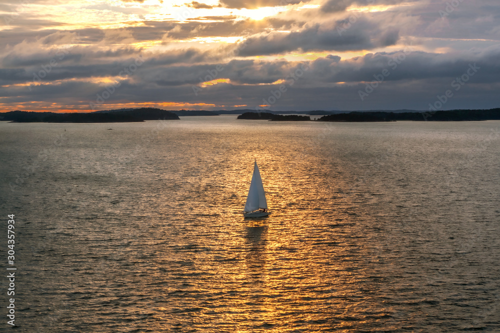 lonely sailboat against the backdrop of the setting sun against the backdrop of the coastline and rainy clouds