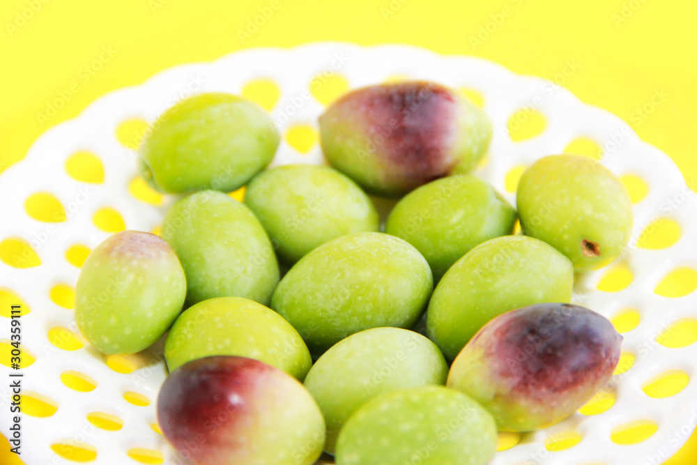 natural green and brown olives in a decorative plate on a yellow background natural green and brown olives in a decorative plate on a yellow background