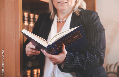 Avvocato donna appoggiata alla libreria che legge un libro  photo