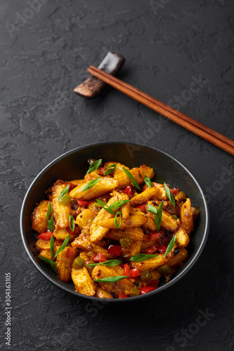 Baby Corn Manchurian dry looks like Schezwan Baby Corn in black bowl at dark slate background. Baby Corn Manchurian - is indo chinese cuisine dish with deep fried corn, bell peppers, sauce and onion.