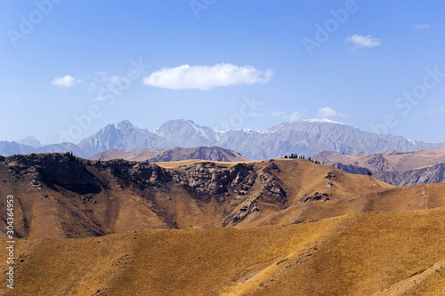Mountains of Kyrgyzstan on a bright sunny day. The mountains like a layered cake are located one after another. Near without stones, like a hill. Far high mountain with snow peaks