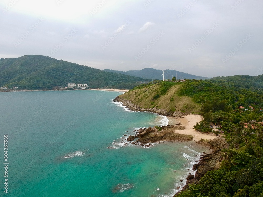 Fototapeta premium Wind turbine Panorama drone aerial view electricity windmill overlooking Naiharn beach phuket Thailand turquoise blue waters white golden sandy beach lush green mountains 