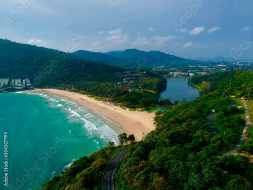 Wind turbine Panorama drone aerial view electricity windmill overlooking Naiharn beach phuket Thailand turquoise blue waters white golden sandy beach lush green mountains 