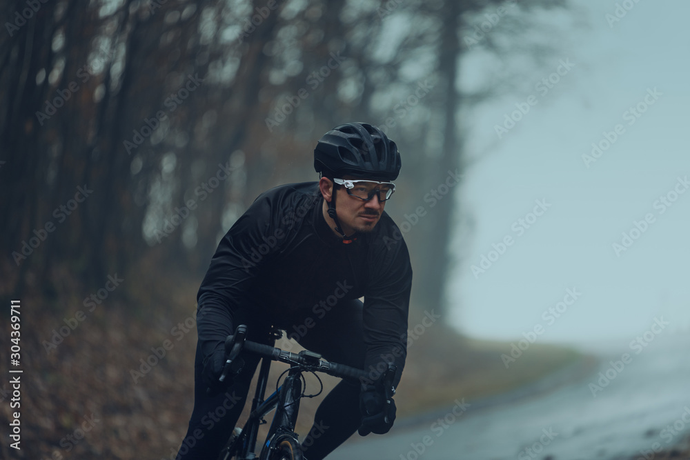 Rennradfahrer im Herbst bei Nebel auf eine Landstraße im Wald Rennradfahrer im Herbst bei Nebel auf eine Landstraße im Wald