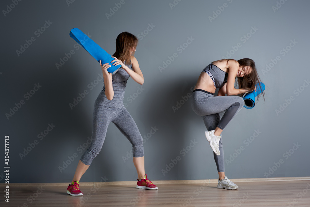 Sporty women fighting twisted blue rugs against gray empty wall