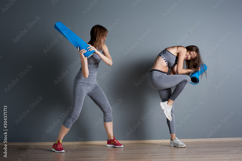 Obraz premium Sporty women fighting twisted blue rugs against gray empty wall