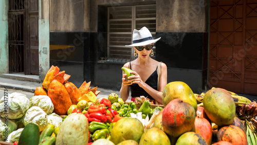 Woman in white hat picks avocado near the counter with vegetables and fruits in the street