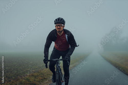 Rennradfahrer bei Nebel im Herbst allein auf einer leeren Landstraße