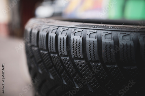 Shallow depth of field (selective focus) image with details of a dirty winter tyre in a car workshop. Sipes and cuts in the tread highlighted.