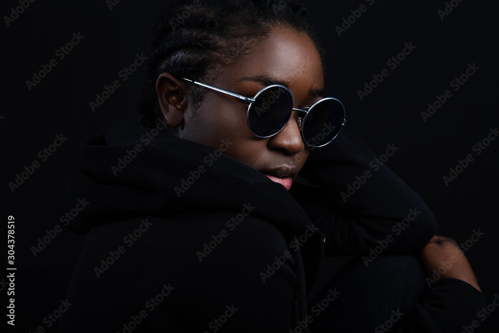 Cool woman sitting with dark skin wearing round sunglasses - obrazy, fototapety, plakaty 