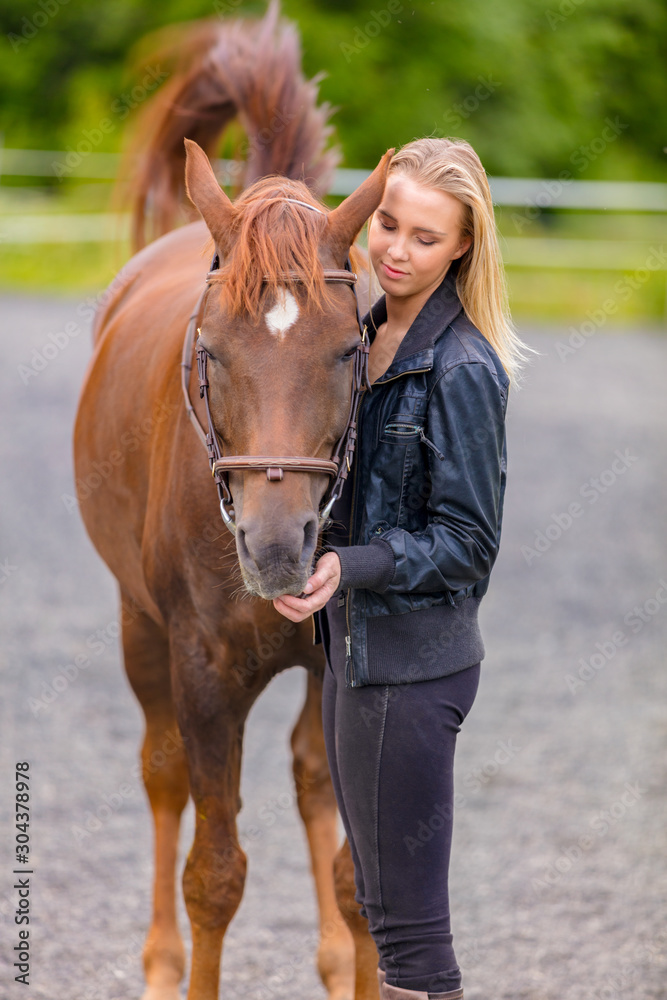 Fototapeta premium Young woman with her arabian horse standing at a riding course