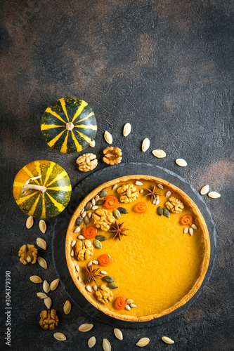 Traditional american homemade holiday pumpkin pie on a dark background with pumpkins top view copy space.