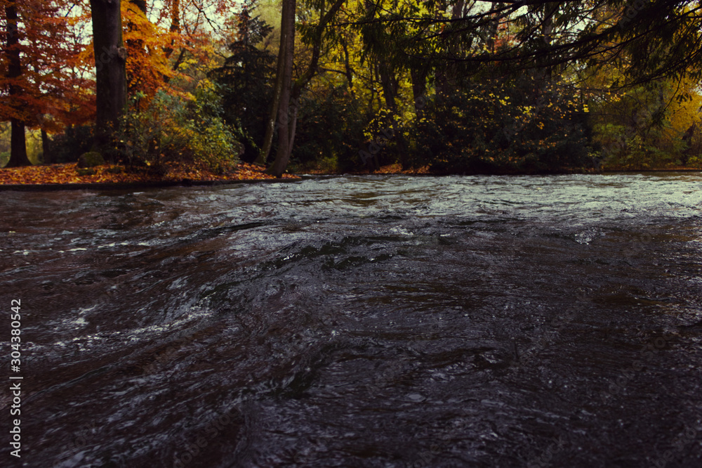 A fast Eisbach stream, river on an autumn, fall day in the Englisher Garten park, Munich, Germany A fast Eisbach stream, river on an autumn, fall day in the Englisher Garten park, Munich, Germany
