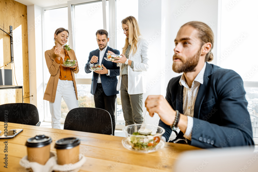 Group of a young office workers eating salads and drinking coffee at the modern office canteen. Concept of a healthy takeaway food on the work Group of a young office workers eating salads and drinking coffee at the modern office canteen. Concept of a healthy takeaway food on the work