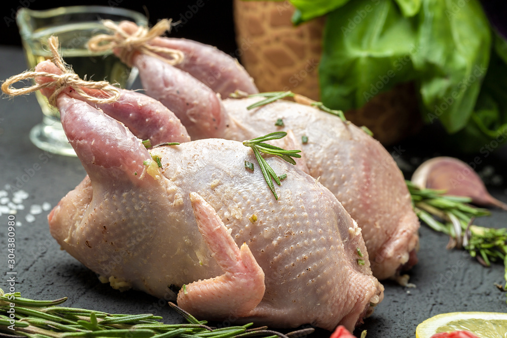 Fresh raw meat quails with herbs and greens rosemary, basil ready for cooking on close-up. Uncooked quail. Cooking poultry meat. Fresh raw meat quails with herbs and greens rosemary, basil ready for cooking on close-up. Uncooked quail. Cooking poultry meat.