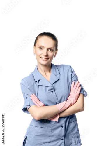 A beautiful young woman in the uniform of a maid smiling crossed her hands in rubber gloves on her chest. Isolated on a white background.