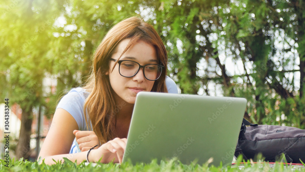 Caucasian teenager girl lying on the grass using laptop. Happiness and lightheartedness concept Caucasian teenager girl lying on the grass using laptop. Happiness and lightheartedness concept