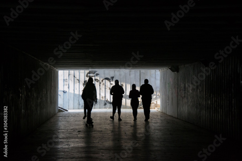 People walking through a dark underpass with glowing end, underground passage, blurred people silhouettes 