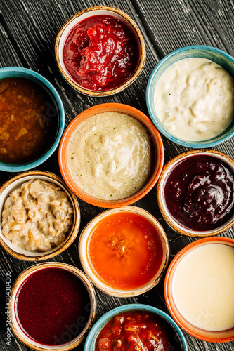 Set of different sauces on black wooden background.