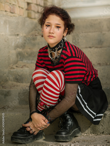 Obraz na plátně Goth emo girl portrait with a skirt, striped stockings and heels boots sitting o