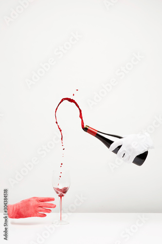 Diner party, an hand whith a white clove is pooring wine in a wine glass.