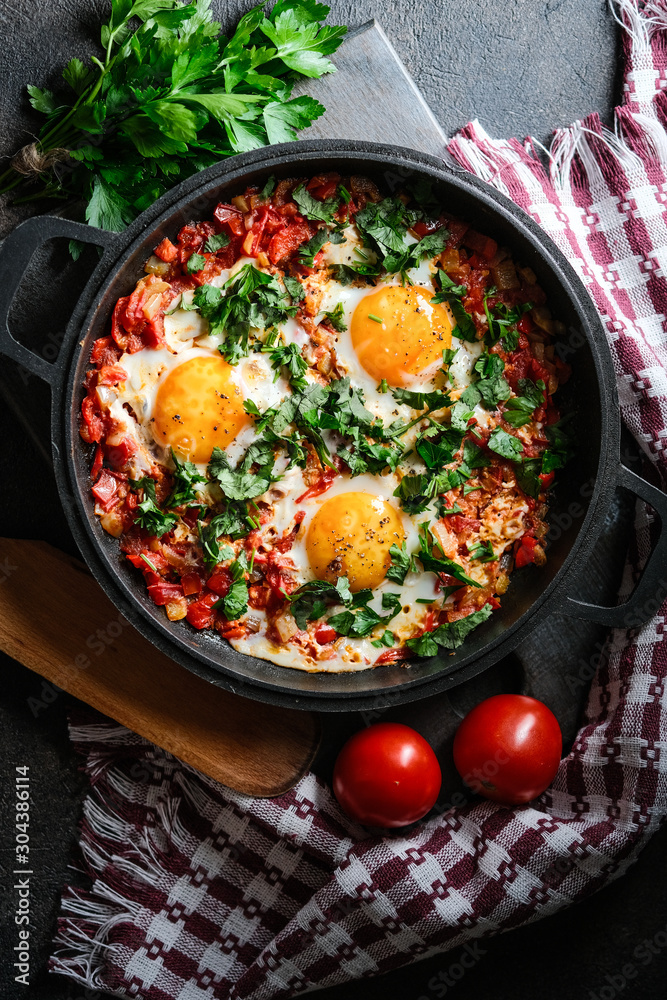 Shakshuka with eggs, tomato, and parsley in a iron pan. Top view copy space