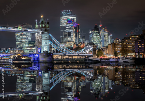 Die beleuchtete City von London und Skyline der Stadt bei Nacht mit Reflektionen im Fluss Themse  Gro  britannien