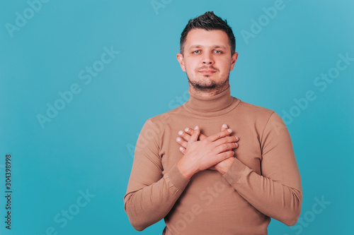 Begging for something. emotional handsome young man puts hands on chest sincerely requesting God posing isolated on blue studio background, man expressing thanks. close up portrait. photo