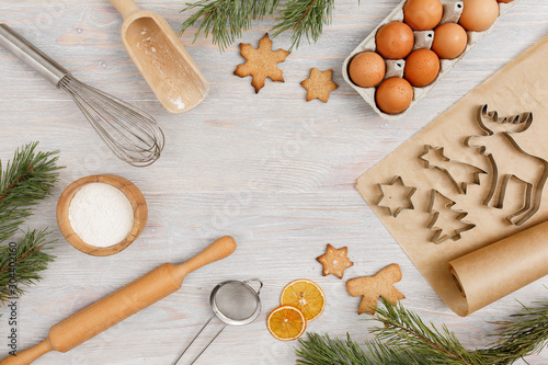 Ingredients and kitchen tools for cooking Christmas baking on light wood table top . Flour, eggs, rolling pin, cutters, sieve etc. Top view with copy space.