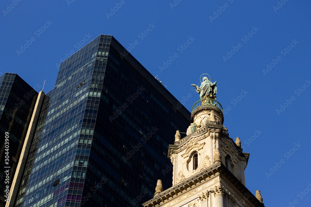 A black business building beside the top of a historic church with a blue sky in Rio de Janeiro downtown, Brazil