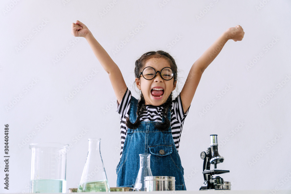 Little 6s cute girl wear glasses happy raise arms with microscope, laboratory bottle and water experiment study scientists while learning success at school. Education science concept. - obrazy, fototapety, plakaty 