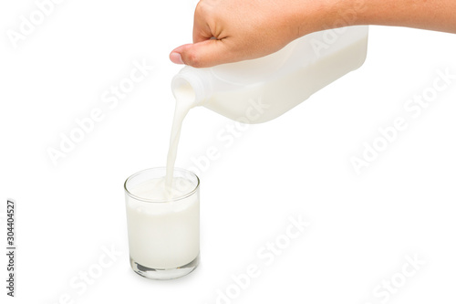 Hand holding Pasteurized fresh milk in a 1 liter plastic gallon while pouring into the glass on white background with clipping path.