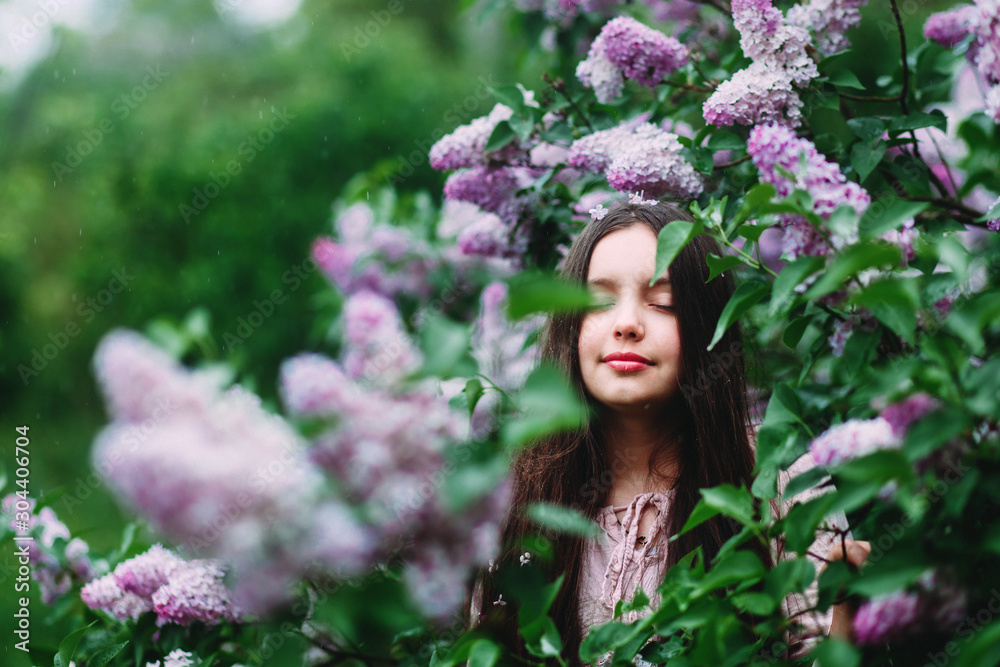 Portrait of a little girl of European appearance against the background of a bush of blooming lilacs in spring. A happy mood in spring Portrait of a little girl of European appearance against the background of a bush of blooming lilacs in spring. A happy mood in spring