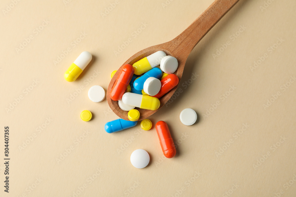 Spoon and pills on beige background, space for text Spoon and pills on beige background, space for text